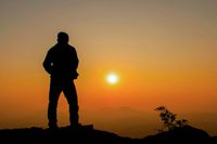 Man standing alone ontop of a rock at sunset